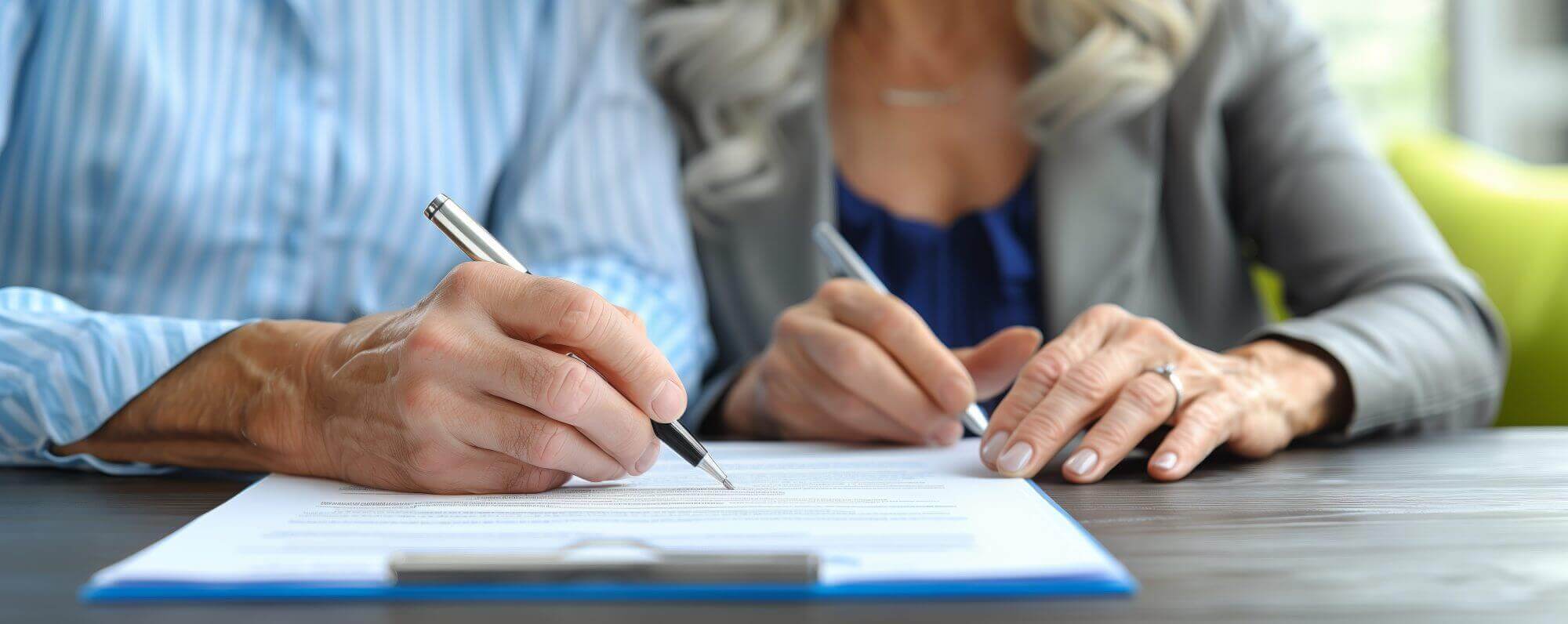 Two people sit at a table, both writing on a document with pens. The focus is on their hands and the paperwork, likely guided by a LaGrange wills attorney to ensure every detail is perfectly captured.