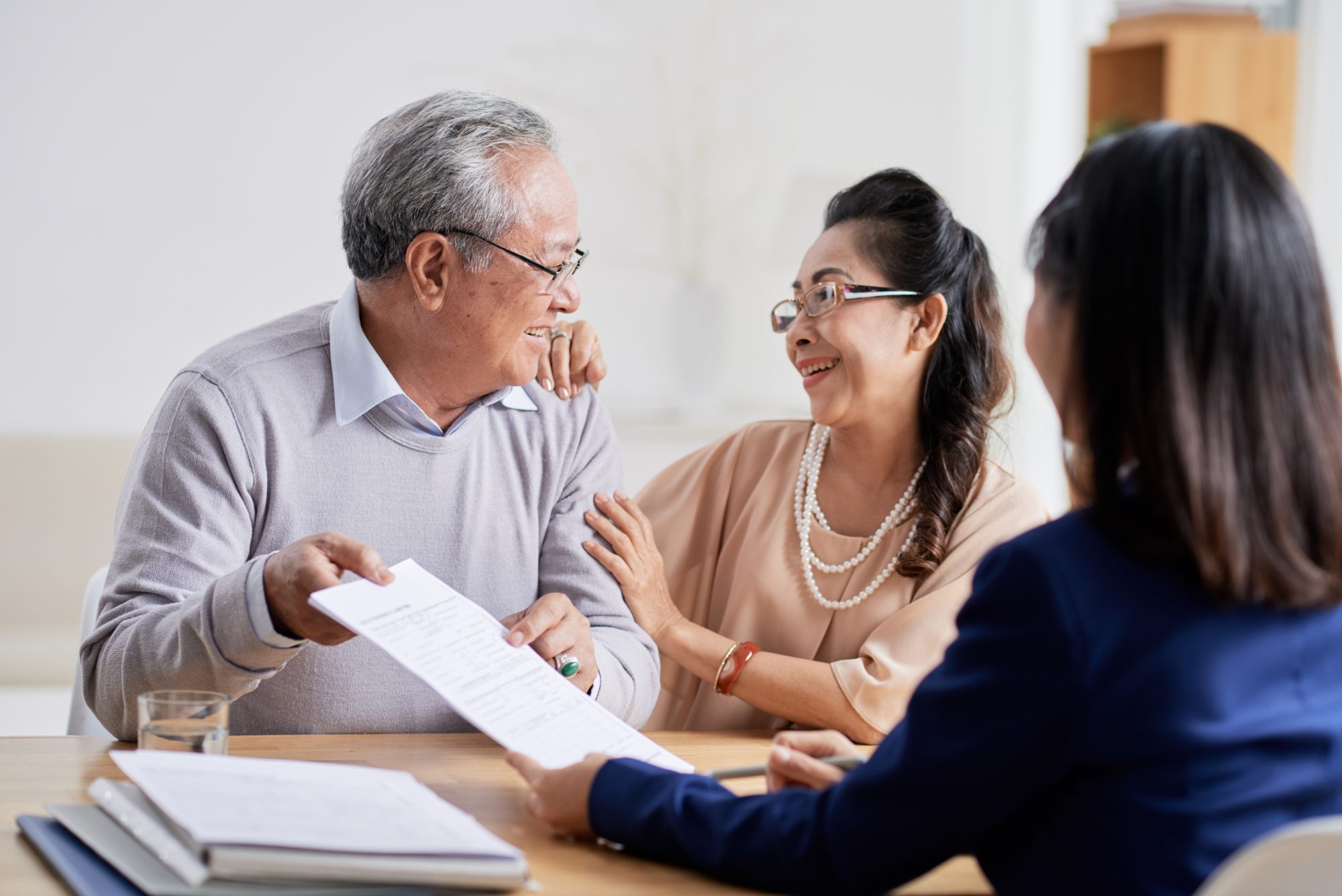 An elderly man and woman smile at each other, holding a document at a table with a professional from Hinsdale Wills.